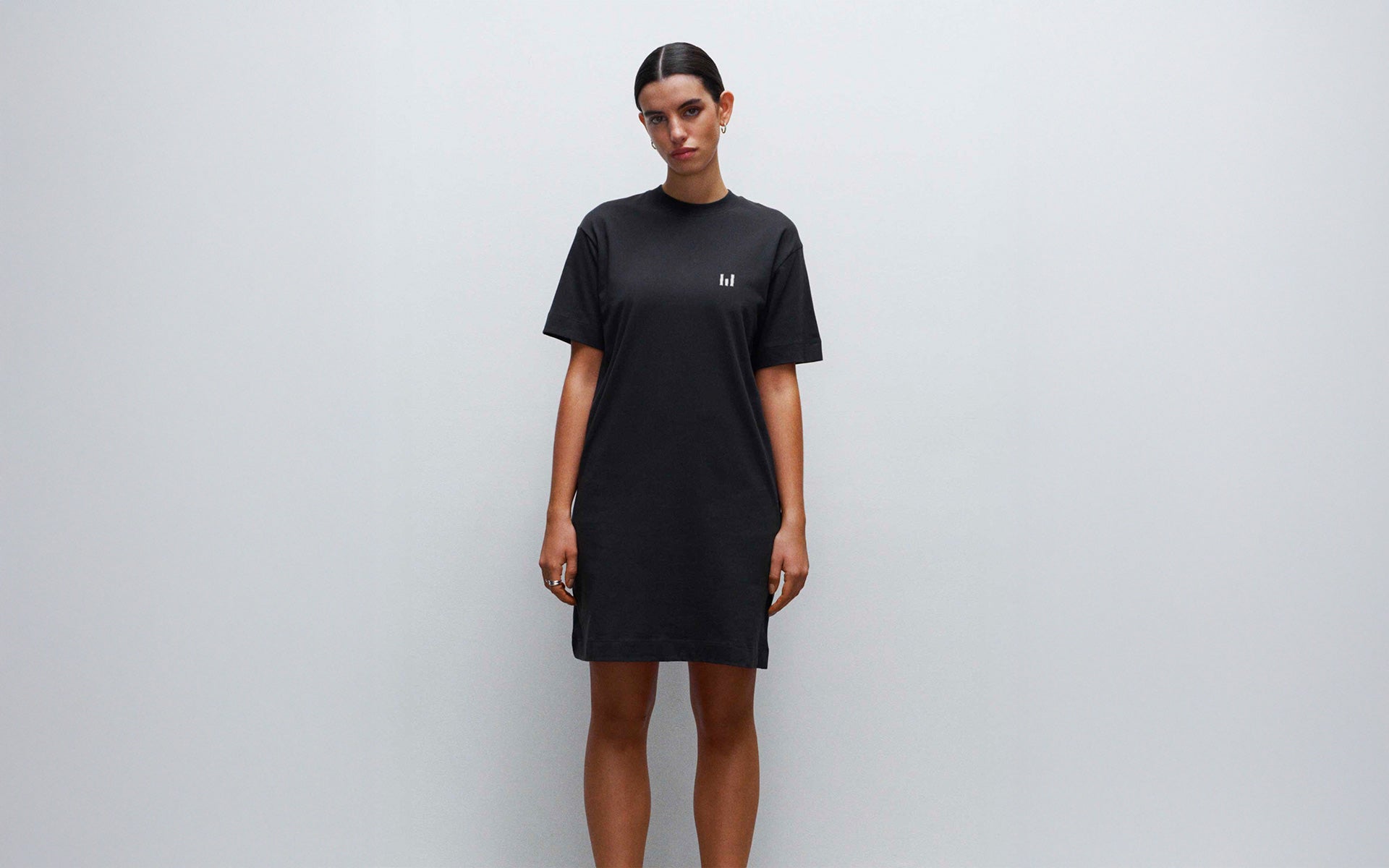 Woman wearing a black t-shirt dress with a small logo on a plain background